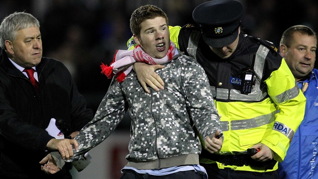 A supporter is led away after running onto the pitch