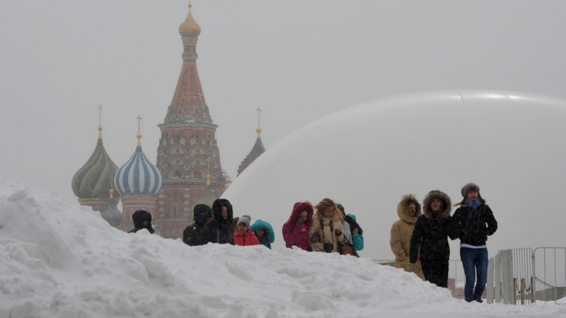 Tourists walk between snowdrifts at the Red Square in Moscow with a huge temporary dome covering the mausoleum of Soviet state founder Vladimir Lenin (R) rising in the background