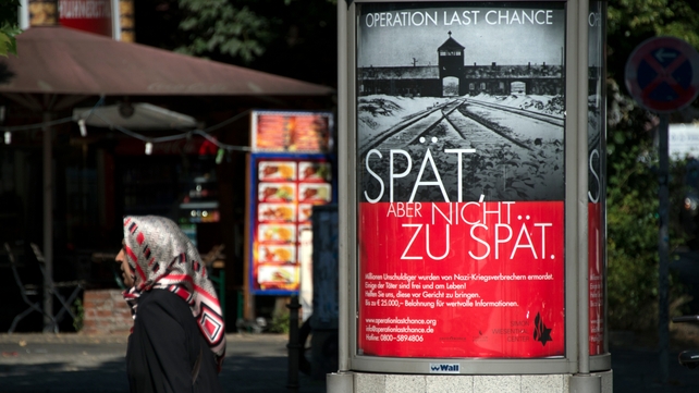 The poster features the infamous gates of Auschwitz along with the slogan 'Late, but not too late' The poster features the infamous gates of Auschwitz along with the slogan 'Late, but not too late'