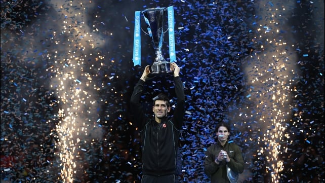 A disconsolate Rafael Nadal looks on as Novak Djokovic holds aloft the Brad Drewett Trophy