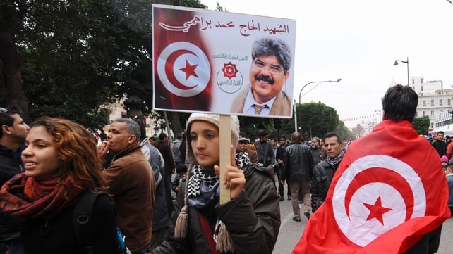 A Tunisian woman holding a placard of portrait of assassinated Tunisian opposition figure Mohamed Brahmi walks past a man wearing the country's national flag A Tunisian woman holding a placard of portrait of assassinated Tunisian opposition figure Mohamed Brahmi walks past a man wearing the country's national flag