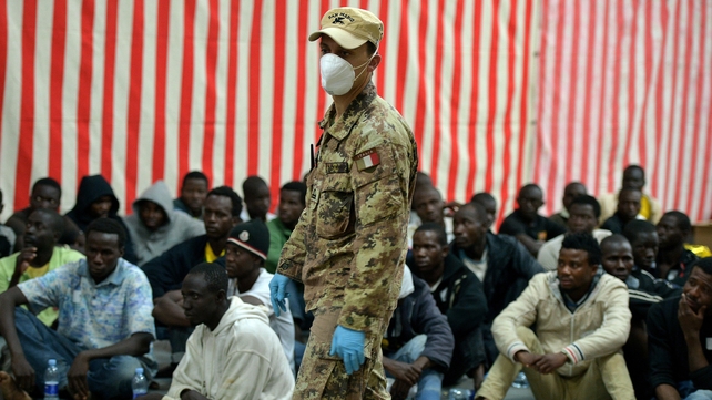A soldier walks past migrants sitting onboard the Italian Navy amphibious assault ship San Marco last year A soldier walks past migrants sitting onboard the Italian Navy amphibious assault ship San Marco last year