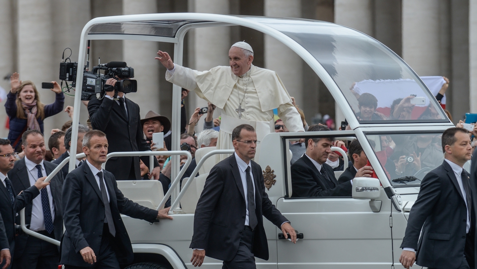 Pope Francis stands on the popemobile surrounded by bodyguards as he waves to pilgrims in St Peter's Square
