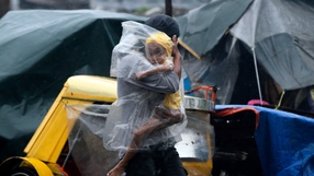 A father with his child covered under a plastic sheet flee the strong winds and rain brought by typhoon Rammasun in Manila