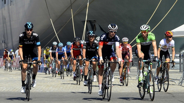 The pack rides past aircraft carrier Juan Carlos I at the Cadiz harbour at the start of the third stage