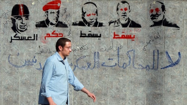 An Egyptian man walks past graffiti depicting members of the military council and reading 