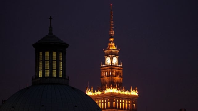 The Palace of Culture and Science (right) stands illuminated behind the Holy Trinity Church of the Augsburg Confession