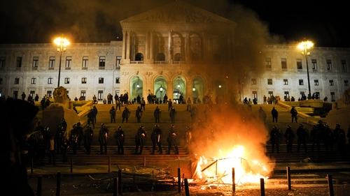 A fire burns as police guard the parliament building in Lisbon