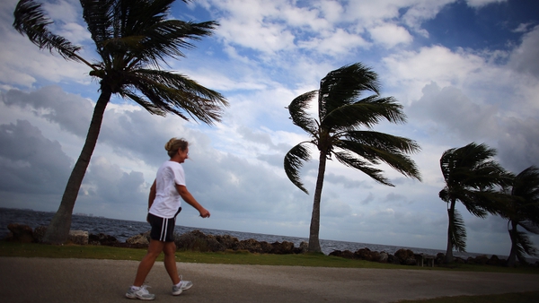 A woman walks along the ocean as blustery winds blow through the palm trees in Miami, Florida