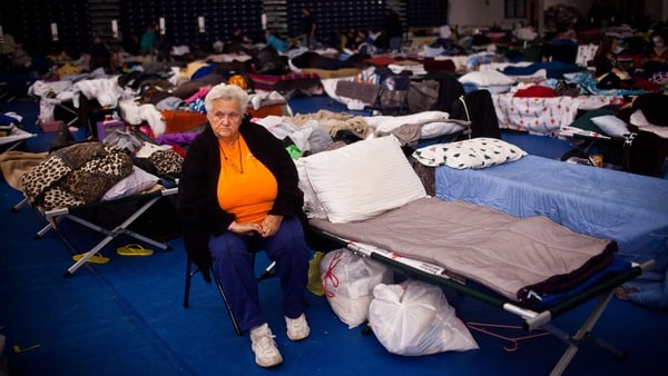 A woman sits next to her bed in a Red Cross evacuation shelter