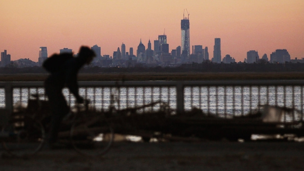 A man bikes past debris in the Rockaway neighbourhood with the Manhattan skyline in the background