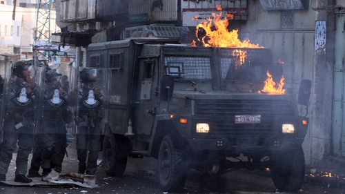 Israeli troops stand by an armoured vehicle that has been attacked by Palestinian protesters
