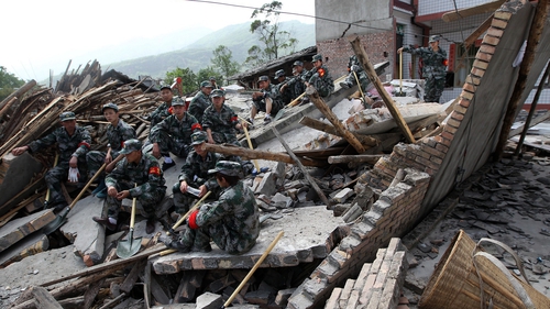 Rescuers sit on ruins of a house in the Longmen area of Sichuan