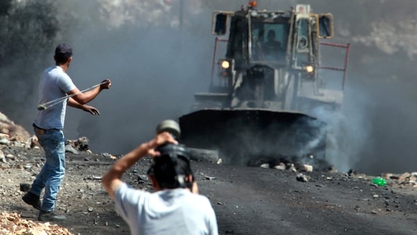 Palestinian protesters throw stones towards an Israeli bulldozer removing a barricade during clashes with security forces near Kfar Qaddum