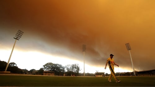 Smoke billows in the background of a cricket match at Drummoyne Oval, north of Sydney