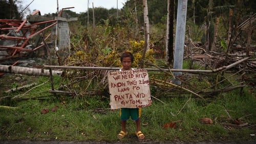 A child holds a placard asking for help by the side of the coastal road in Eastern Samar