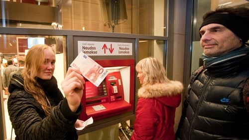 A woman shows a €10 note after withdrawing it from a cash machine in Riga