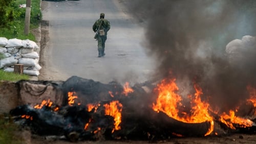 An armed pro-Russian rebel walks behind a burning barricade on a checkpoint in Slaviansk