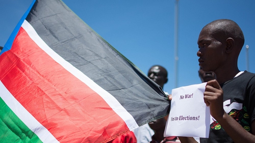 A South Sudanese man holds a placard reading 'No to War, Yes to Elections!' and the country's flag