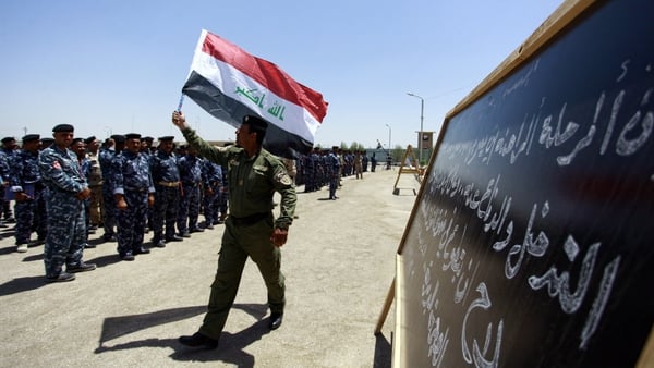 A member of Iraq's security forces wave his national flag as newly recruited men gather
