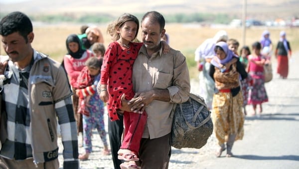 A displaced Iraqi man from the Yazidi community carries his daughter as they cross the Iraqi-Syrian border