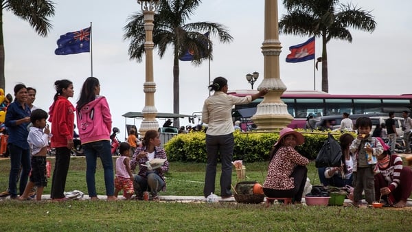 A group of street food sellers interact with Cambodian customers on the riverside in front of the Cambodian and the Australian flags in Phnom Penh