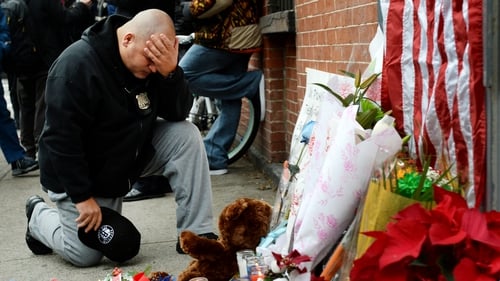 An NY police officer says a prayer while kneeling in front of memorial for the two deceased officers