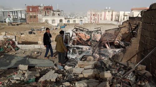 Two men stand near a burnt-out car amid the wreckage close to the presidential palace