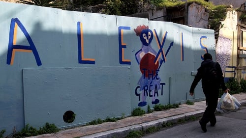 A man passes by a wall covered with graffiti reading 'Alexis the Great' in central Athens