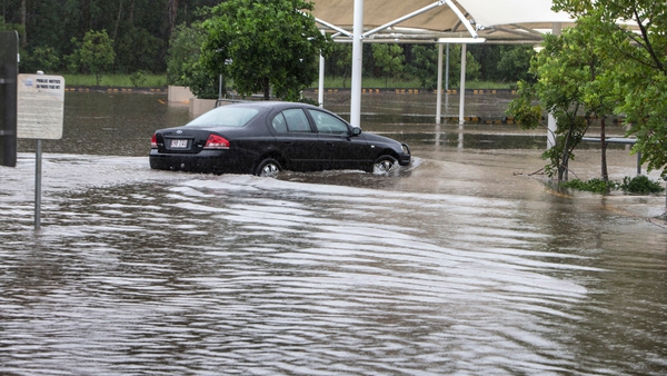 A car drives through flood water in a shopping centre carpark in Brisbane