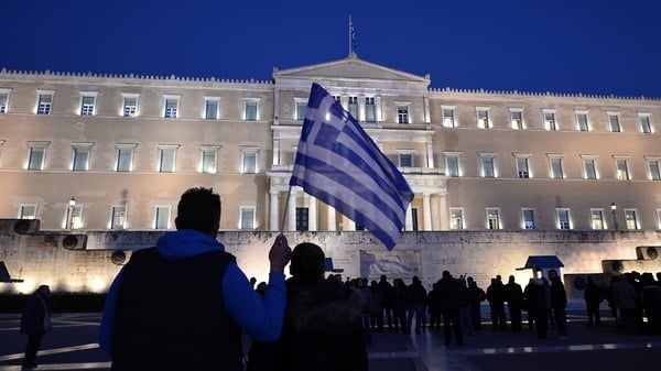 A man holds a Greek flag in front of the Greek parliament in Athens as people gather in support of their government