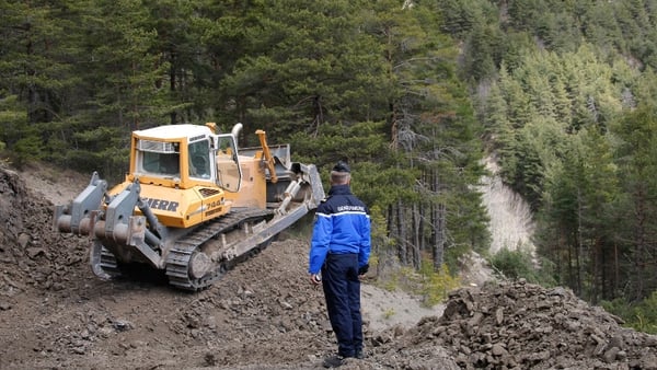 A gendarme watches a bulldozer clearing a path to the crash site near Seyne-les-Alpes