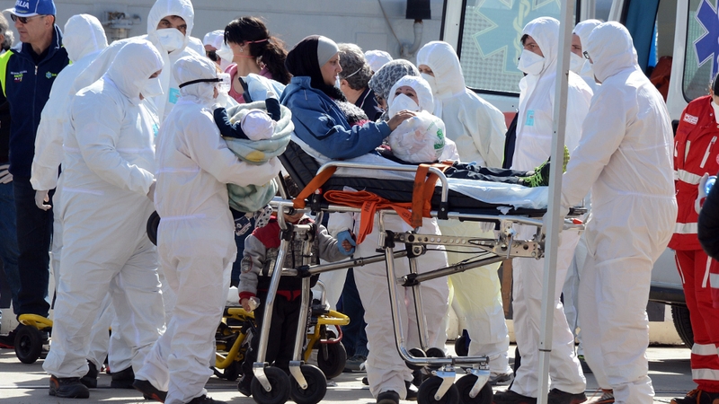 A woman and baby are helped disembark from an Italian navy vessel after a rescue at sea