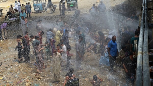 Youths cool themselves from a leaking water pipeline during the heatwave in Karachi