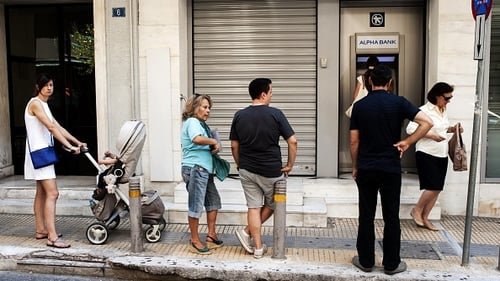People wait in line to withdraw cash from an ATM machine in Athens