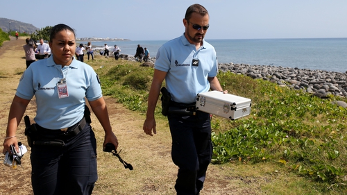Police officers leave the scene with container holding metallic debris found on a beach on Reunion