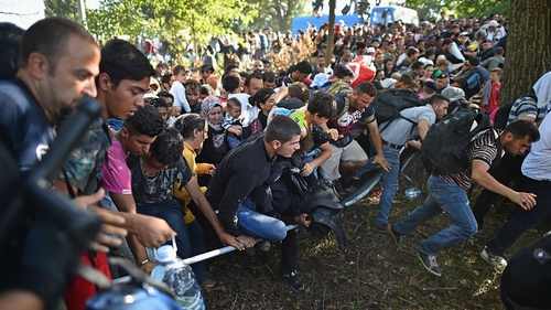 Migrants force their way through police lines at Tovarnik station to board a train bound for Croatia