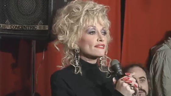 Dolly Parton makes an impromptu appearance at Páidí Ó Sé's pub in Dún Chaoin, County Kerry and takes to the stage to entertain the locals. (1990)