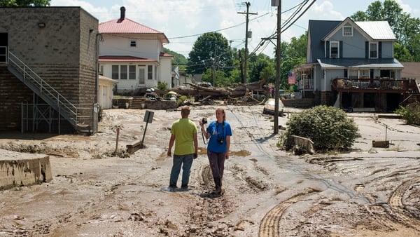 People stand in the middle of a mud-covered street after flooding from the Elk River in Clendenin, West Virginia