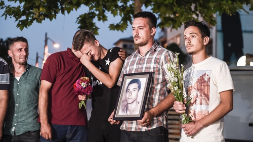 People mourn in Pristina, Kosovo, as they hold flowers and a picture of Diamant Zabergja, one of the victims that was shot dead in the Munich attack