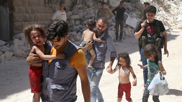 Syrian men carry injured children amid the rubble of destroyed buildings following air strikes on Aleppo