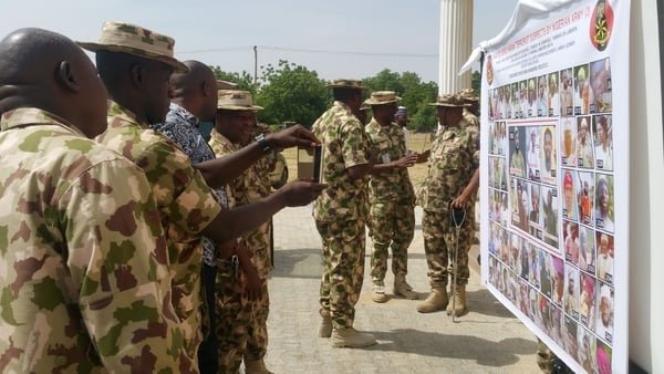 Soldiers take pictures of a banner showing the most wanted Boko Haram members in Maiduguri
