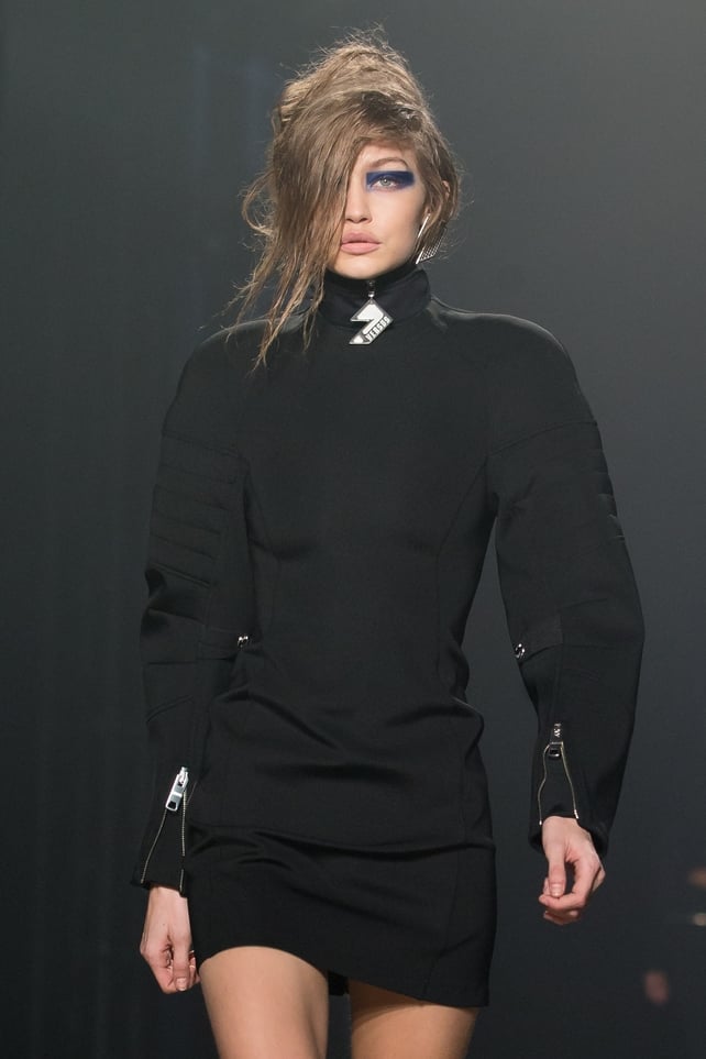Gigi Hadid at the Versus fashion show wearing a textured black dress and blue stripes on her eyes. We hardly recognize her!