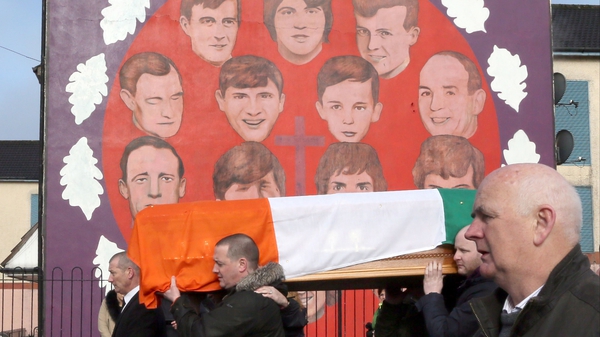 The coffin of Martin McGuinness is carried in procession past a mural in the Bogside