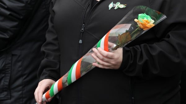 A mourner carries a single rose with the colours of the Tricolour