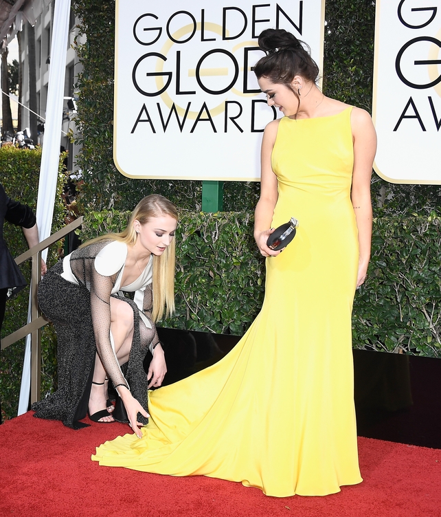 Sophie, while wearing Louis Vuitton, helped Maisie fluff out her yellow Ong-Oaj Pairam gown at the 74th Annual Golden Globes.