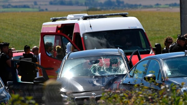 French police officers and emergency workers are seen beside the damaged car