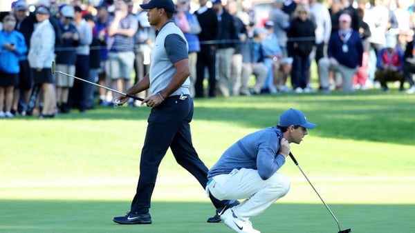 Rory McIlroy (R) lines up a putt on the 14th green beside Tiger Woods