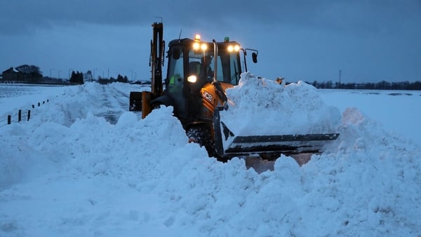 A digger works into the evening to clear snow from the A905