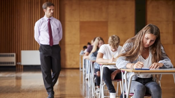 Teenage Students Sitting Examination With Teacher Invigilating